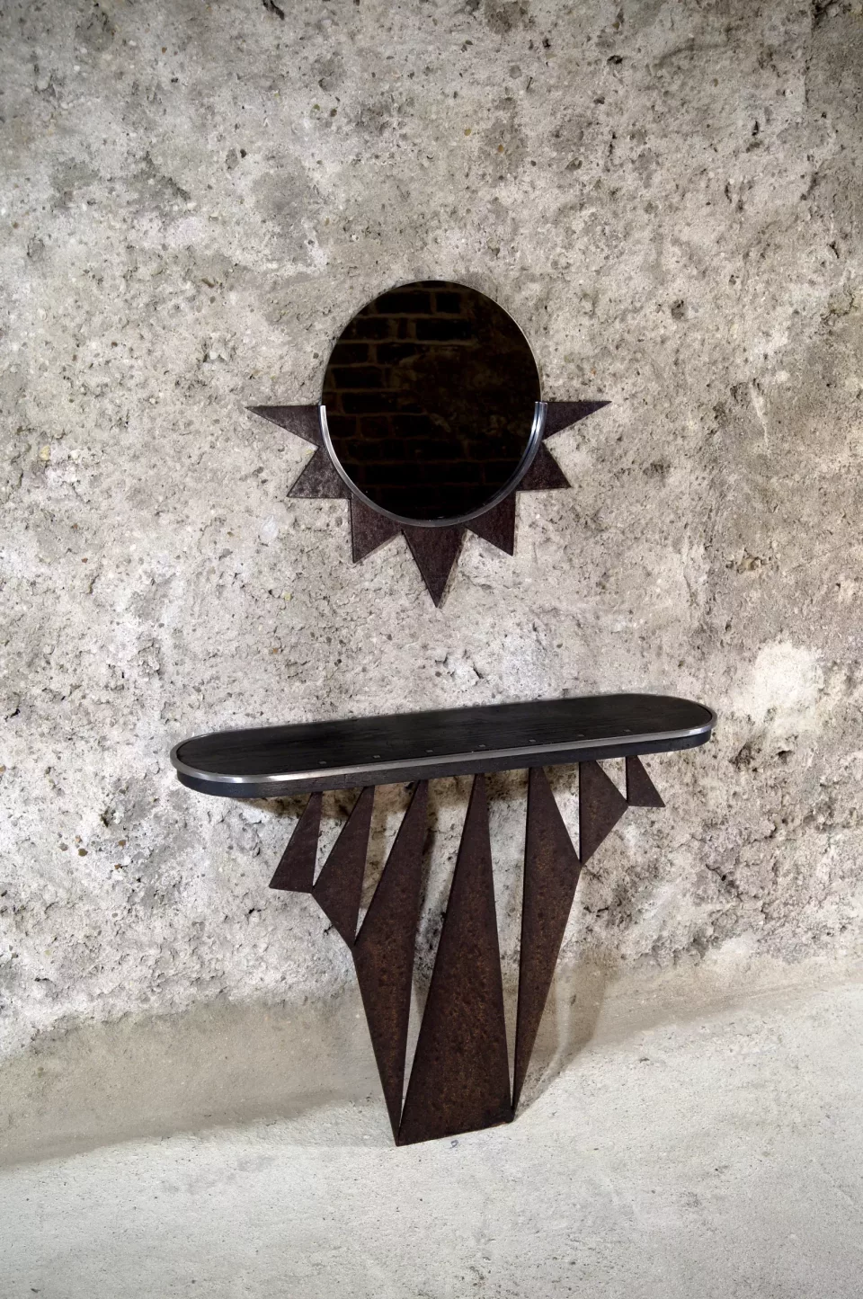 Console en bois brûlé aux pieds découpés en flammes, plateau sombre, surmontée d’un miroir rond à rayons.