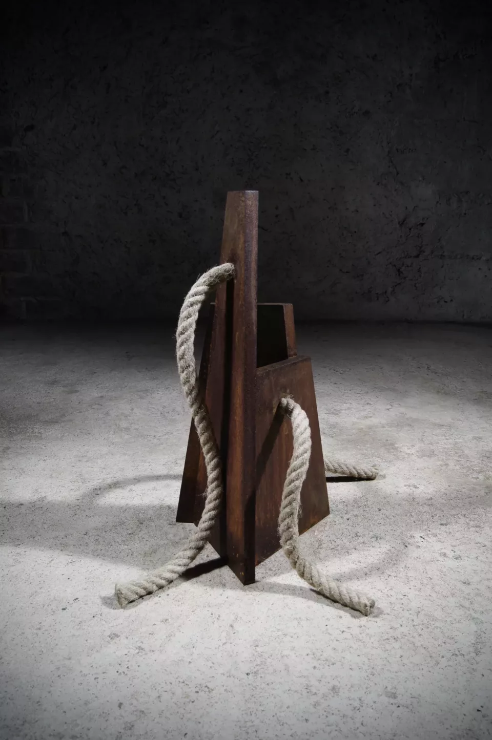 Vase trapézoïdal en acier rouillé, entouré d’une corde de chanvre enroulée au sol.