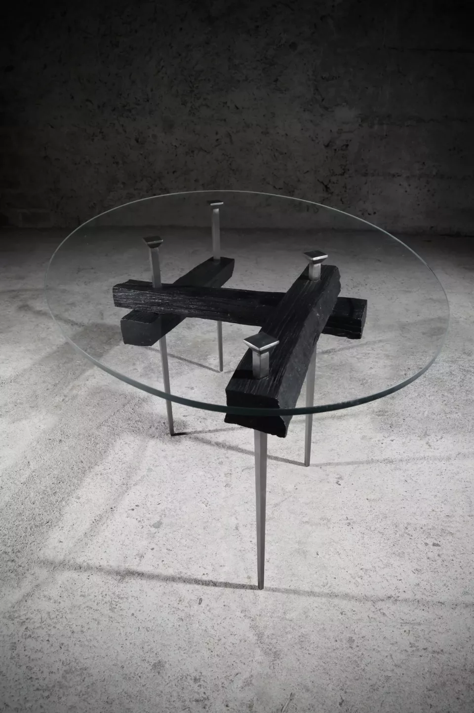 Table basse à plateau de verre rond posé sur un socle d’acier noir en croix hérissée de pointes.