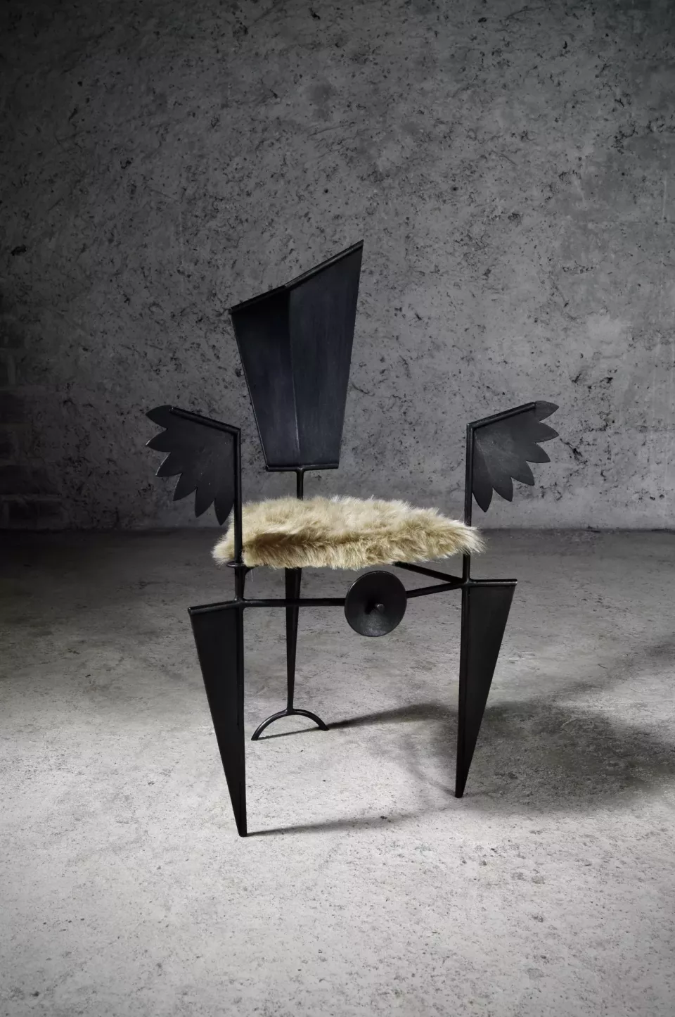 Chaise en acier peint noir au dossier en ailes anguleuses, assise garnie de fourrure claire.