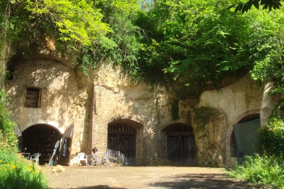 Cour troglodyte creusée dans la falaise, arches de pierre et feuillages : le décor des photographies.
