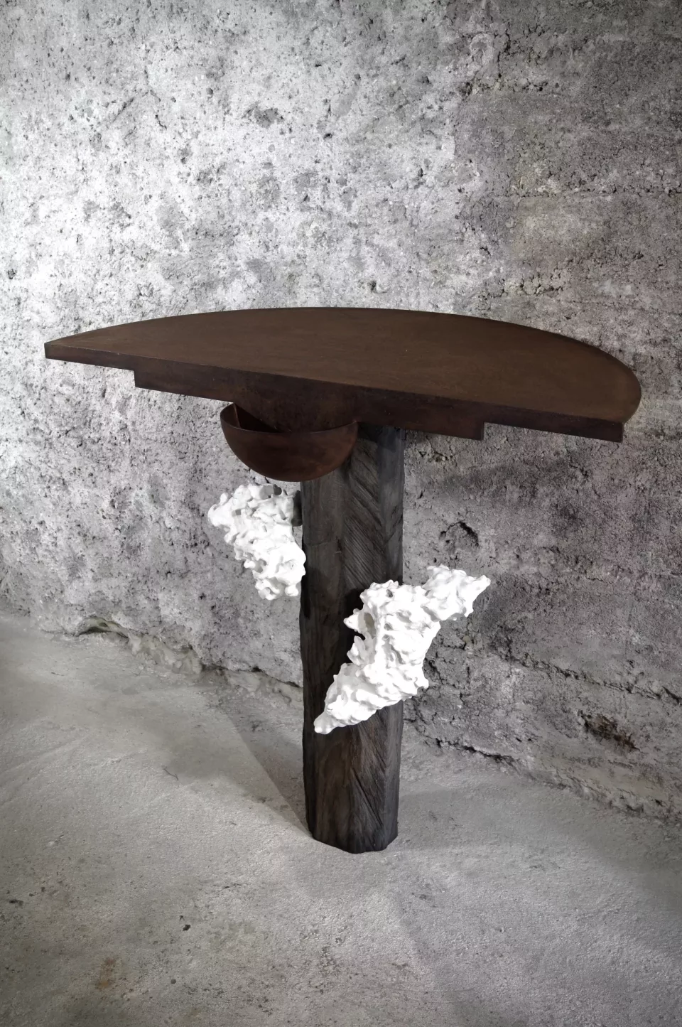Console demi-lune en bois tronçonné sombre, fût massif orné d’un corail fossile blanc.