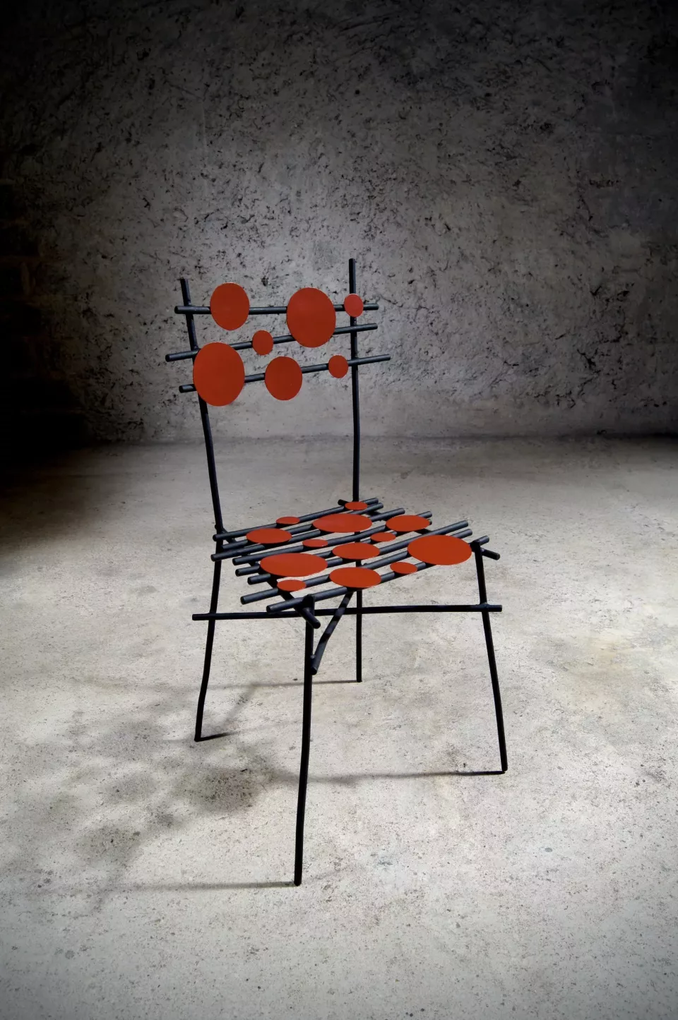 Chaise en acier peint noir semée de pastilles rouges, assise tressée orange.