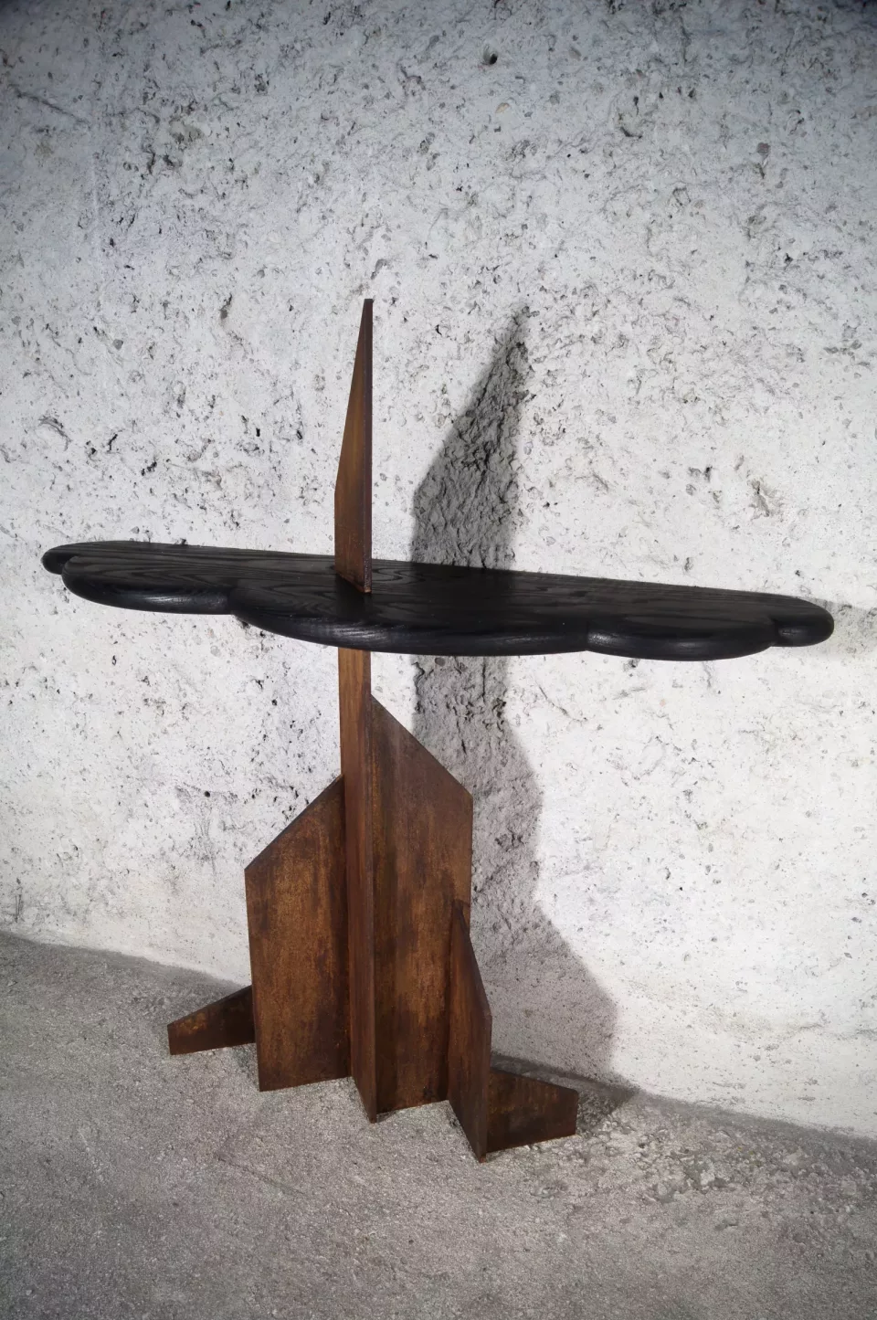 Console à plateau ovale sombre posé sur un socle anguleux de frêne brûlé et d’acier rouillé.