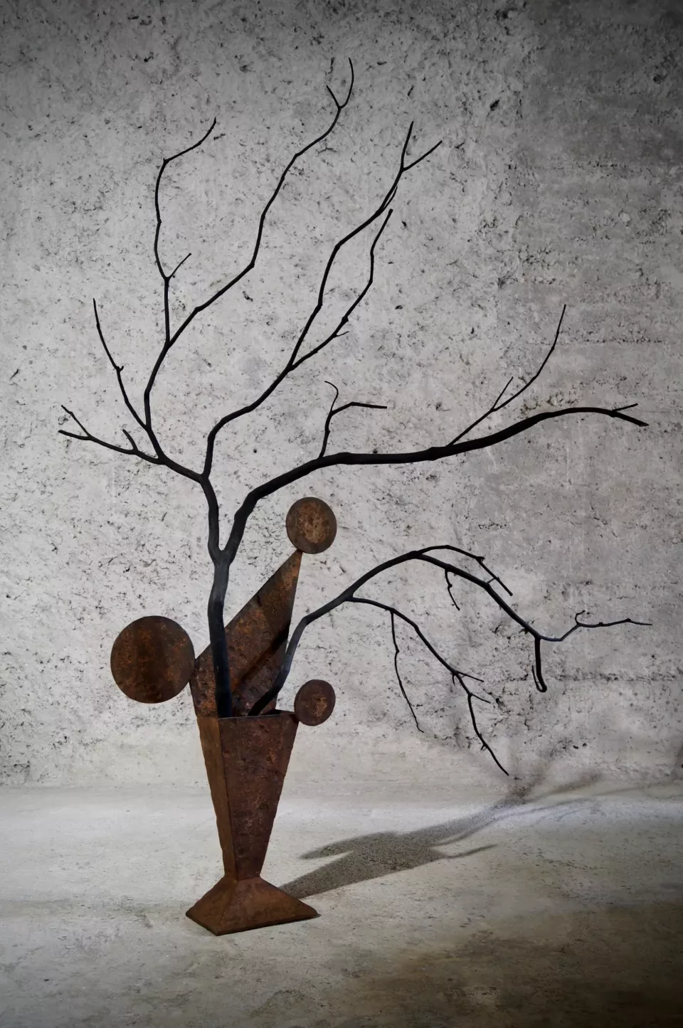 Vase conique en acier rouillé, garni de branches noires nues et de disques de rouille.